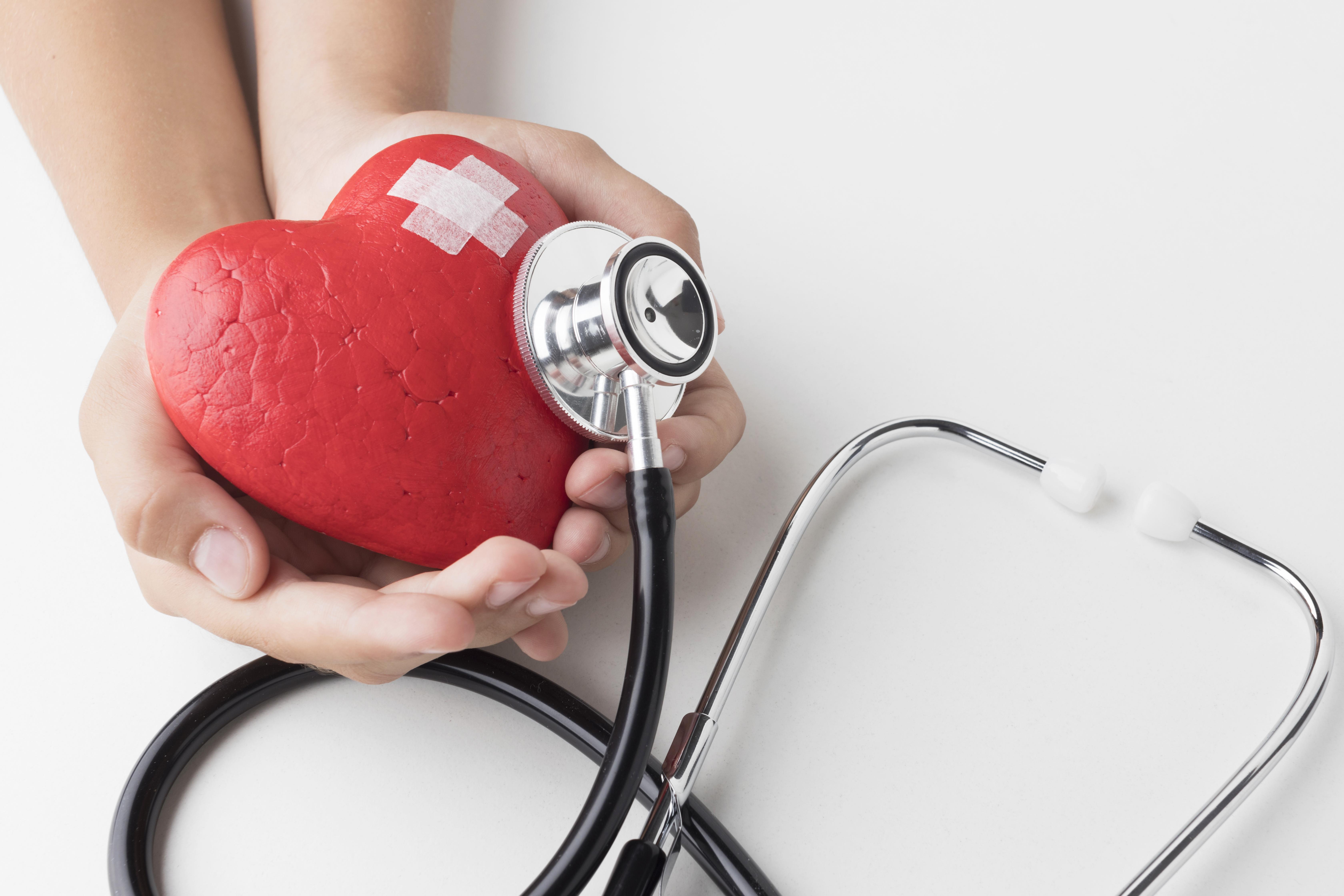 Hands holding a red heart with a stethoscope pressed against it, symbolizing the connection between sleep apnea and heart health.